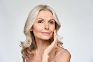 Secondary image for 5 Signs You Would Benefit from a Facial Fat Transfer. Lovely older woman touching cheek